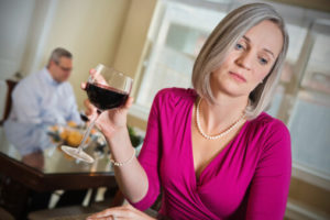 alcoholic wife holding a glass of wine while husband works in the background