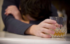 man holding a drink with his head down on the table - how to tell if you're a drunk